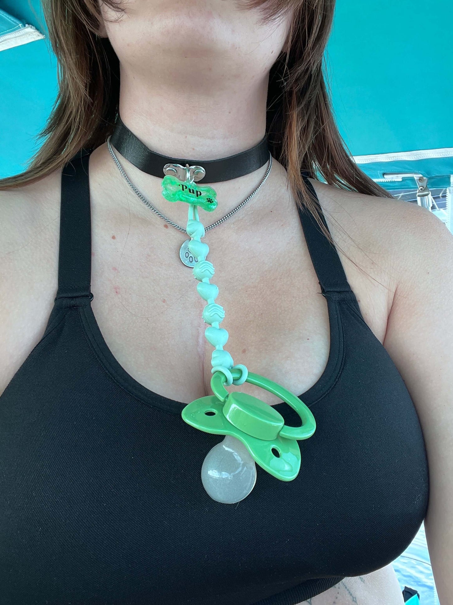 Adult pacifier choker featuring a comfortable choker with an attached adult pacifier, connected by a chewable silicone string. A customizable resin name tag is displayed at the center for personalization.