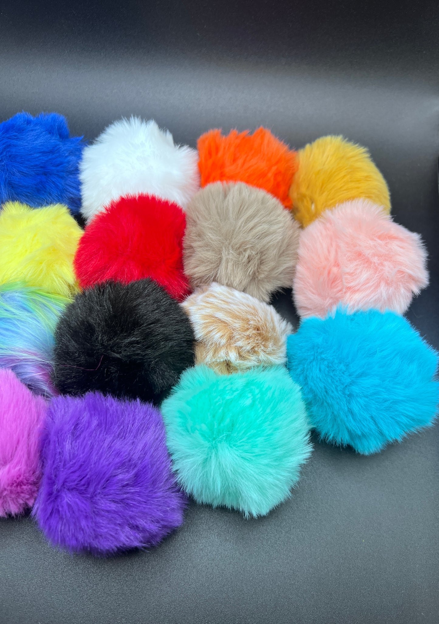 Assorted colorful fluffy pom-poms on a gray surface