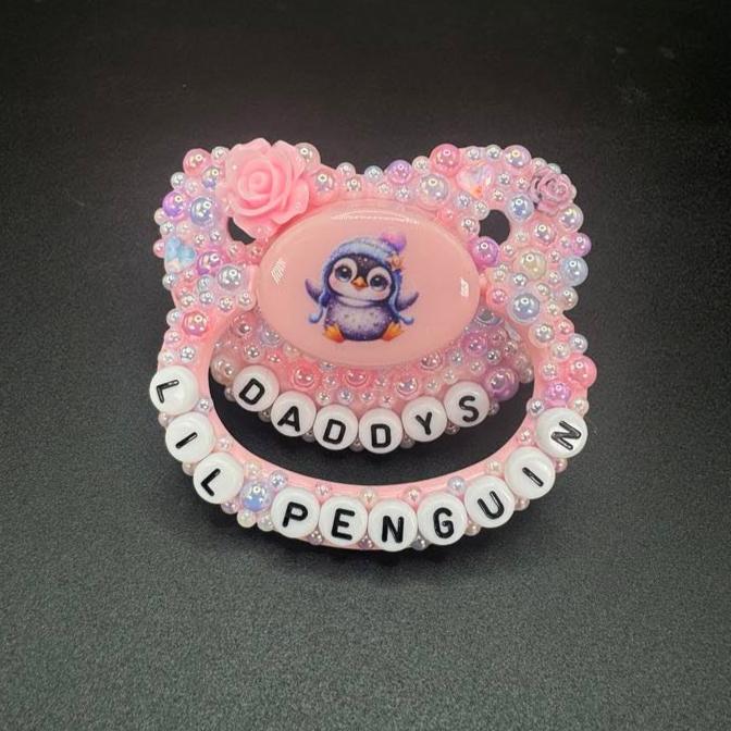 Handmade penguin deco adult pacifier with pastel pearls and the text 'Daddy's Lil Penguin' for playful vibes.