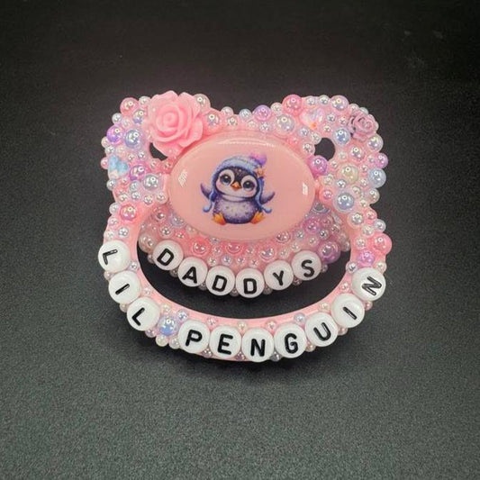 Handmade penguin deco adult pacifier with pastel pearls and the text 'Daddy's Lil Penguin' for playful vibes.