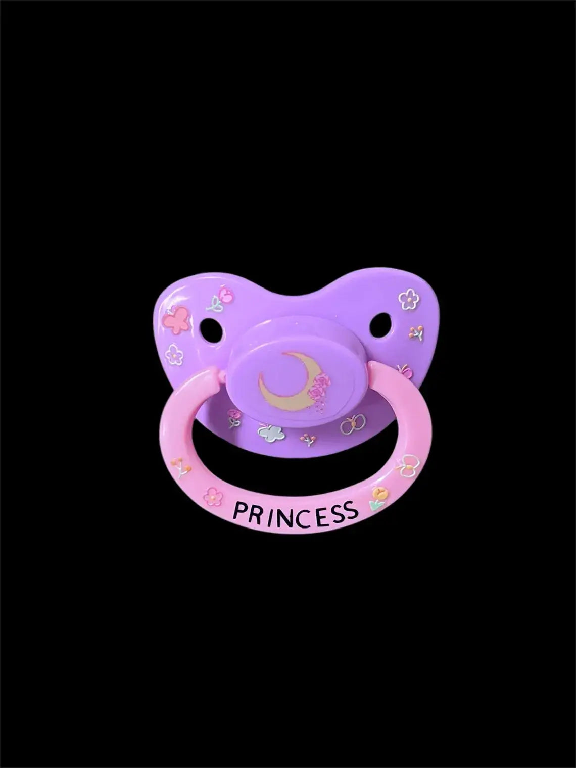 Adult deco pacifier featuring glow-in-the-dark flowers and butterflies on the shield, a moon centerpiece, and the word 'Princess' on the handle for a magical and elegant design.