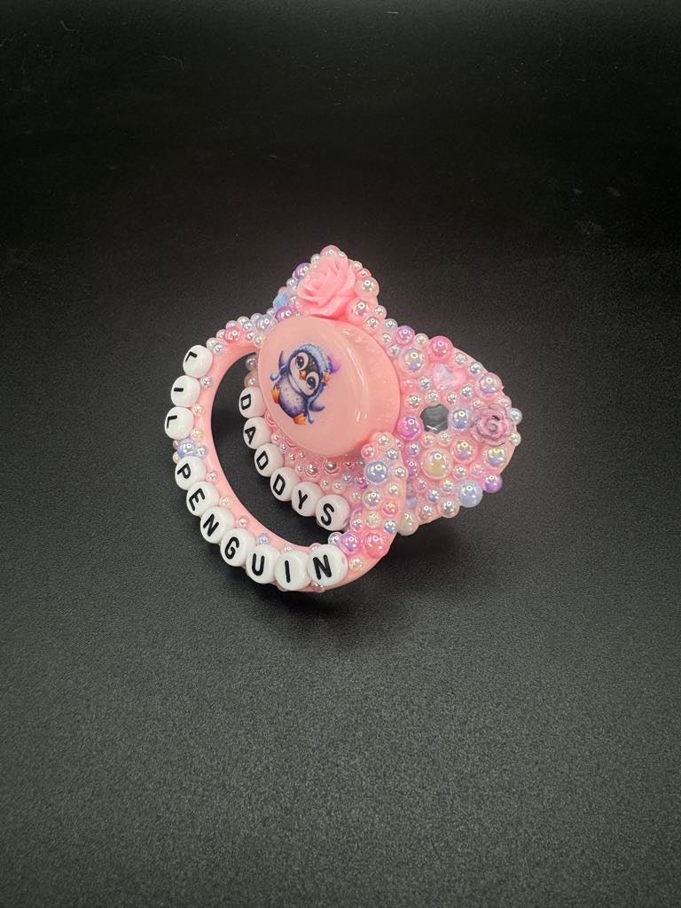 Handmade penguin deco adult pacifier with pastel pearls and custom lettering, perfect for personality and fun.