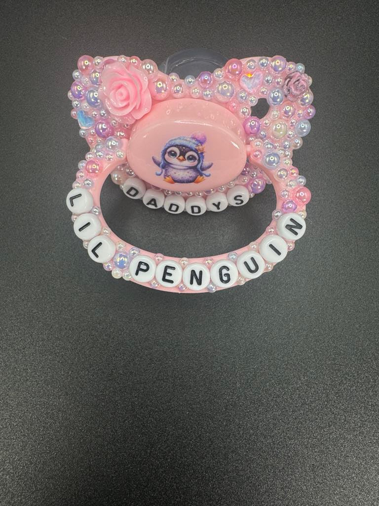 Handmade penguin deco adult pacifier decorated with pearls and tiny flowers, featuring 'Daddy's Lil Penguin' design.