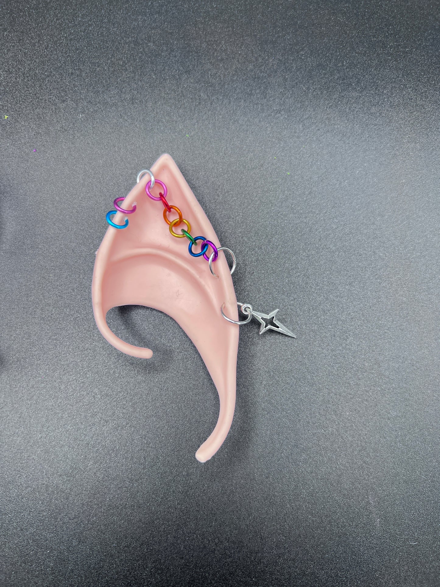 LGBTQ fantasy elf ear with colorful chain details on a gray background
