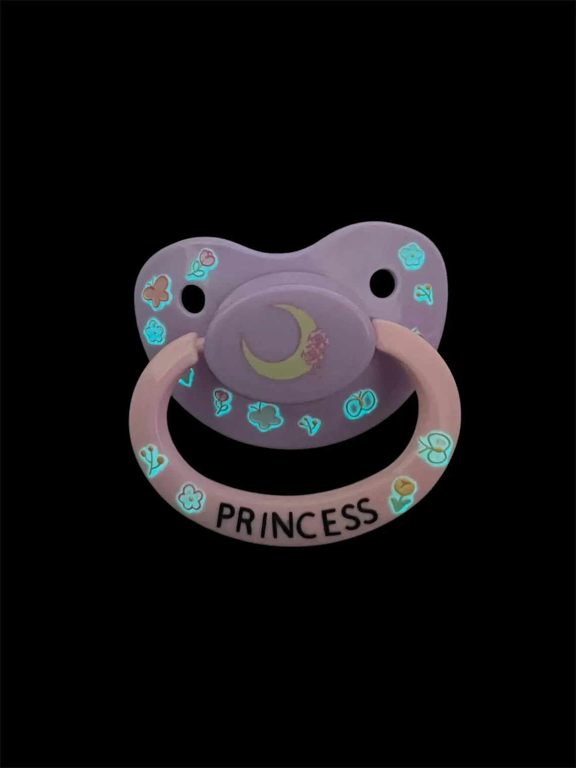 Adult deco pacifier featuring glow-in-the-dark flowers and butterflies on the shield, a moon centerpiece, and the word 'Princess' on the handle for a magical and elegant design.