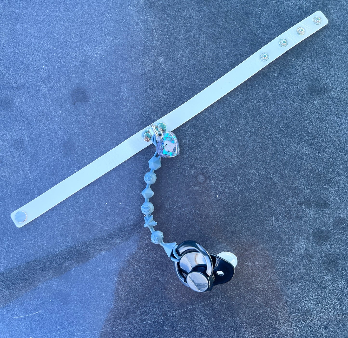 white faux leather choker with ghost resin charm in the center with teether string coming off the center holding an adult pacifier at the end.