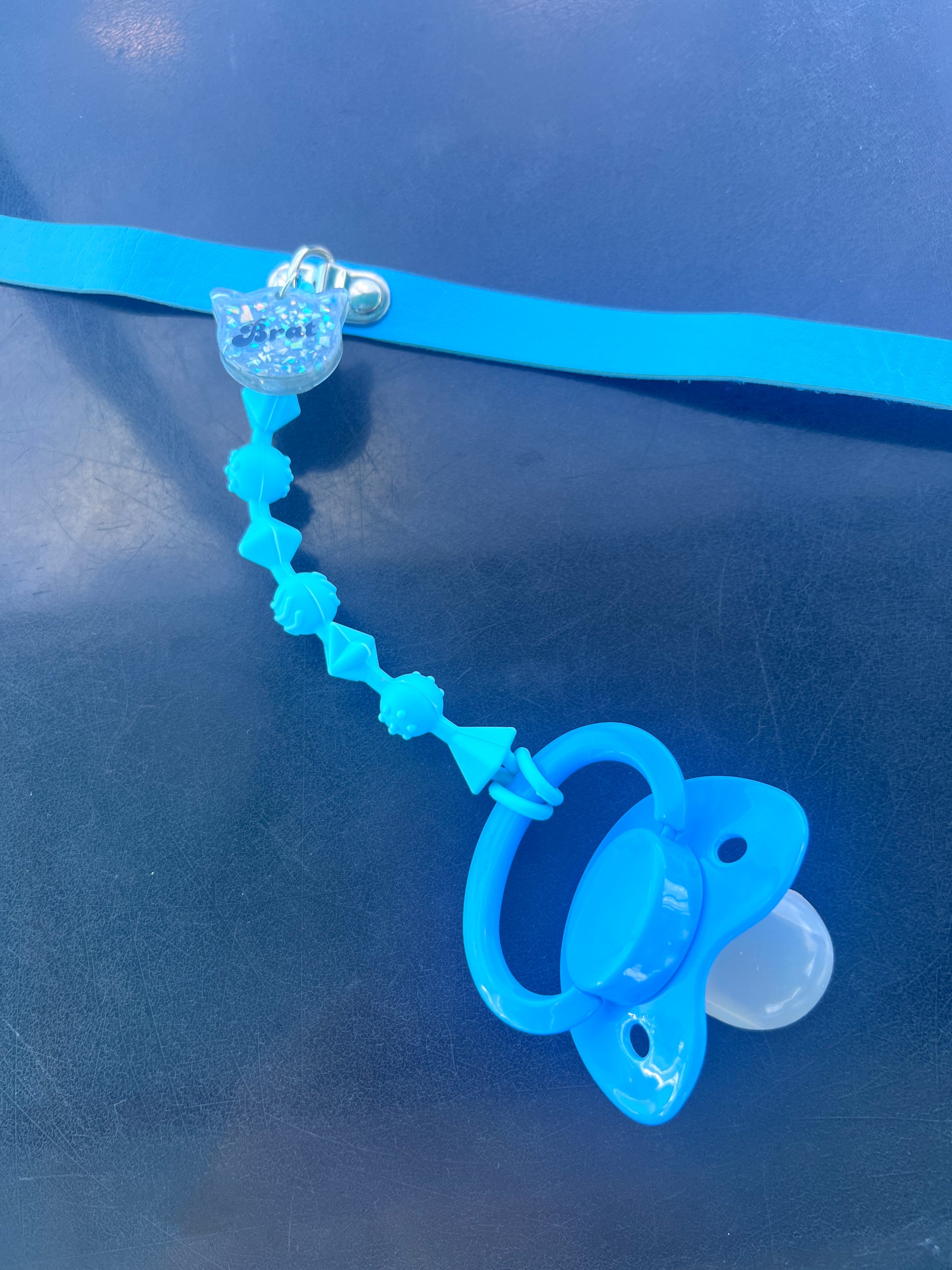 Age regression pacifier collar in soft blue with chew-safe strap and brat tag