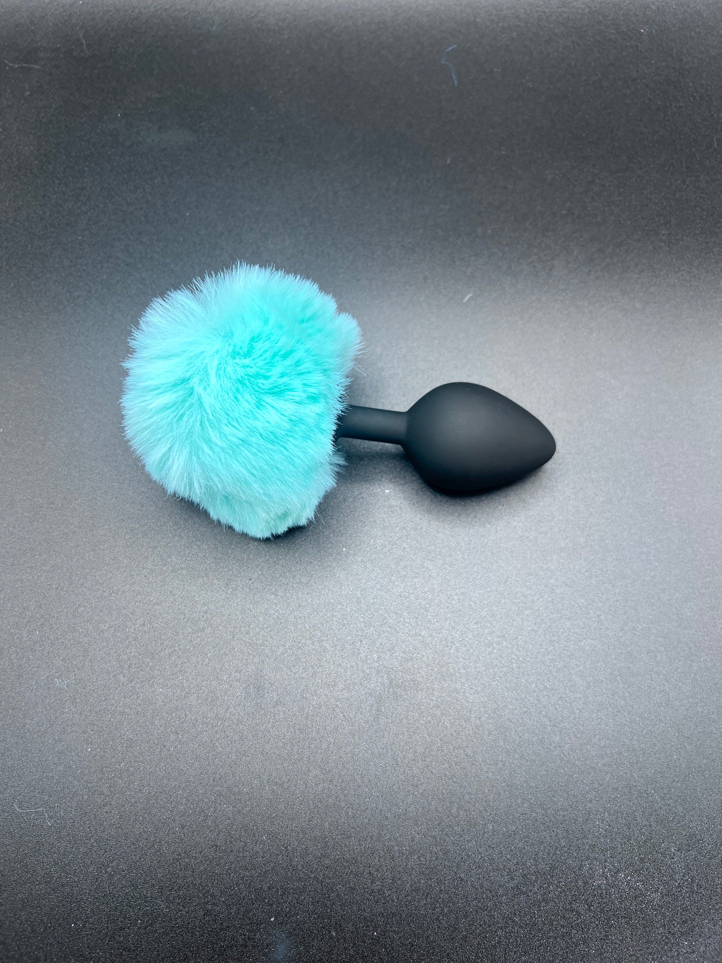 Black butt plug with a turquoise fur bunny tail on a gray background
