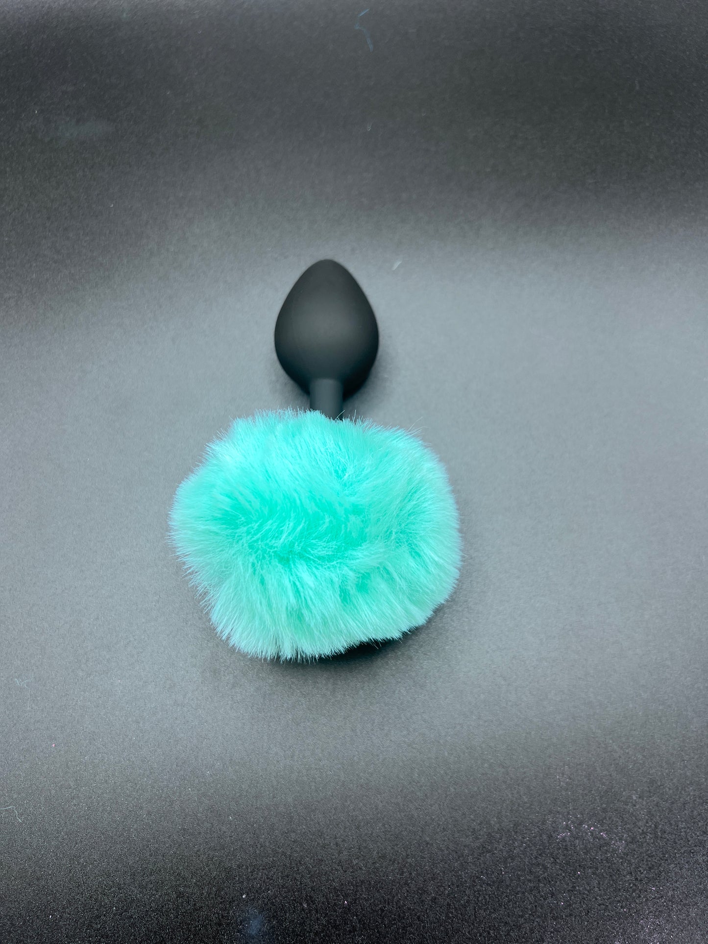 Black butt plug with a teal fur cover on a gray background