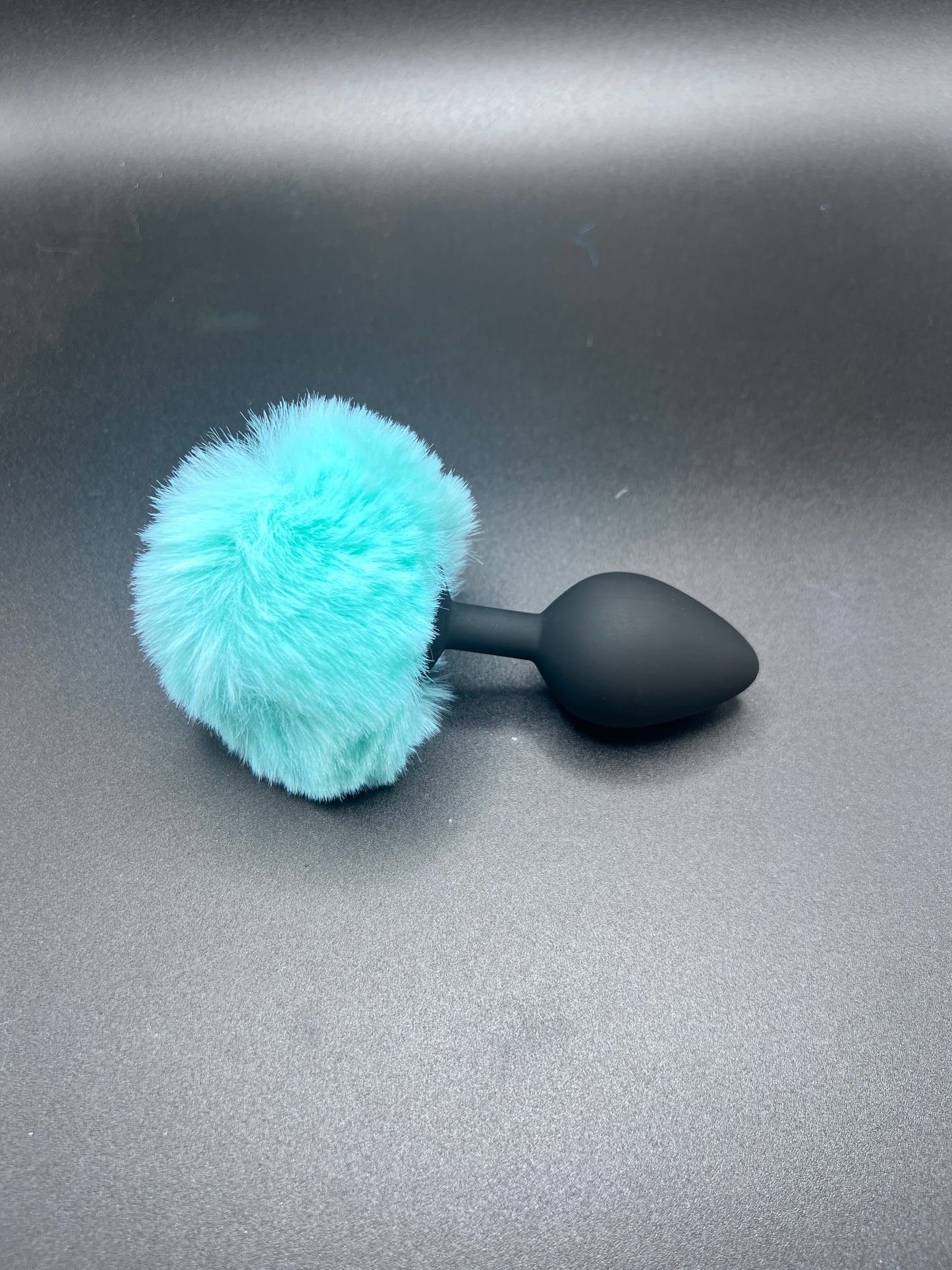 Black bunny anal toy with a turquoise fuzzy ball on a gray background