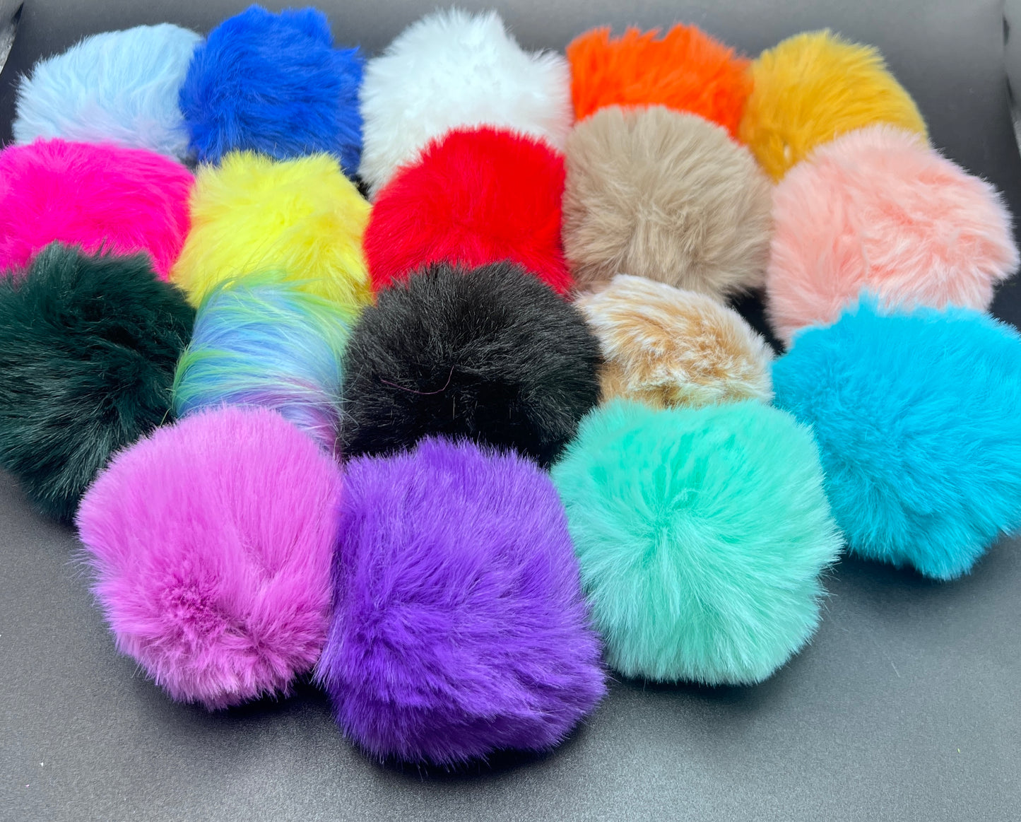 Assorted colorful fluffy pom-poms on a gray background