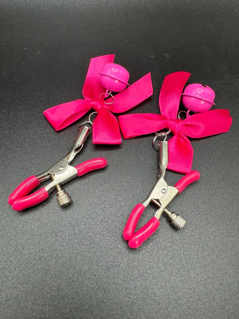 Stainless steel nipple clamps with attached bows and bells at the ends, featuring a silicone cover for added comfort and a stylish, playful touch.