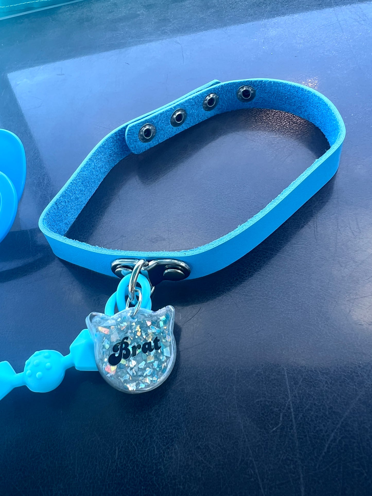Close-up of baby blue pacifier choker with glitter resin charm labeled "Brat"