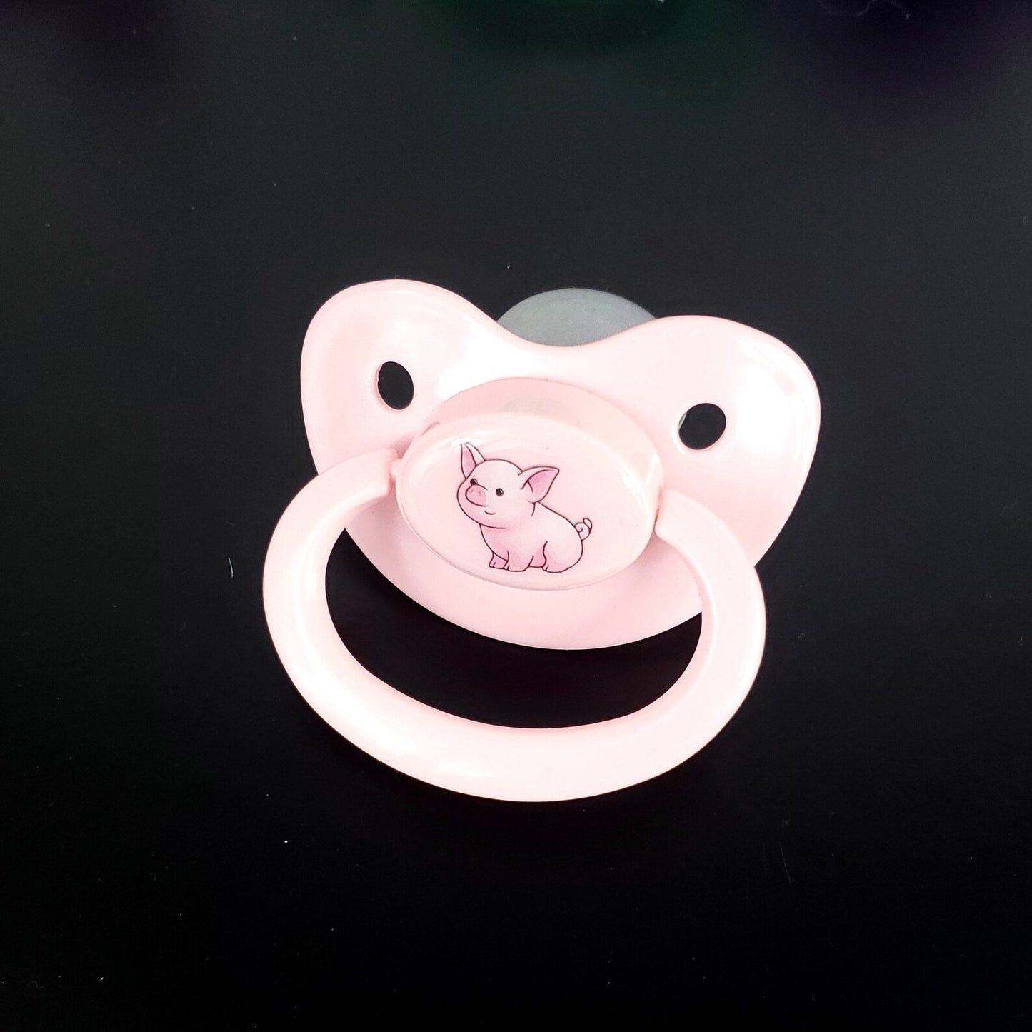 Pink pacifier with a pig design on a black background