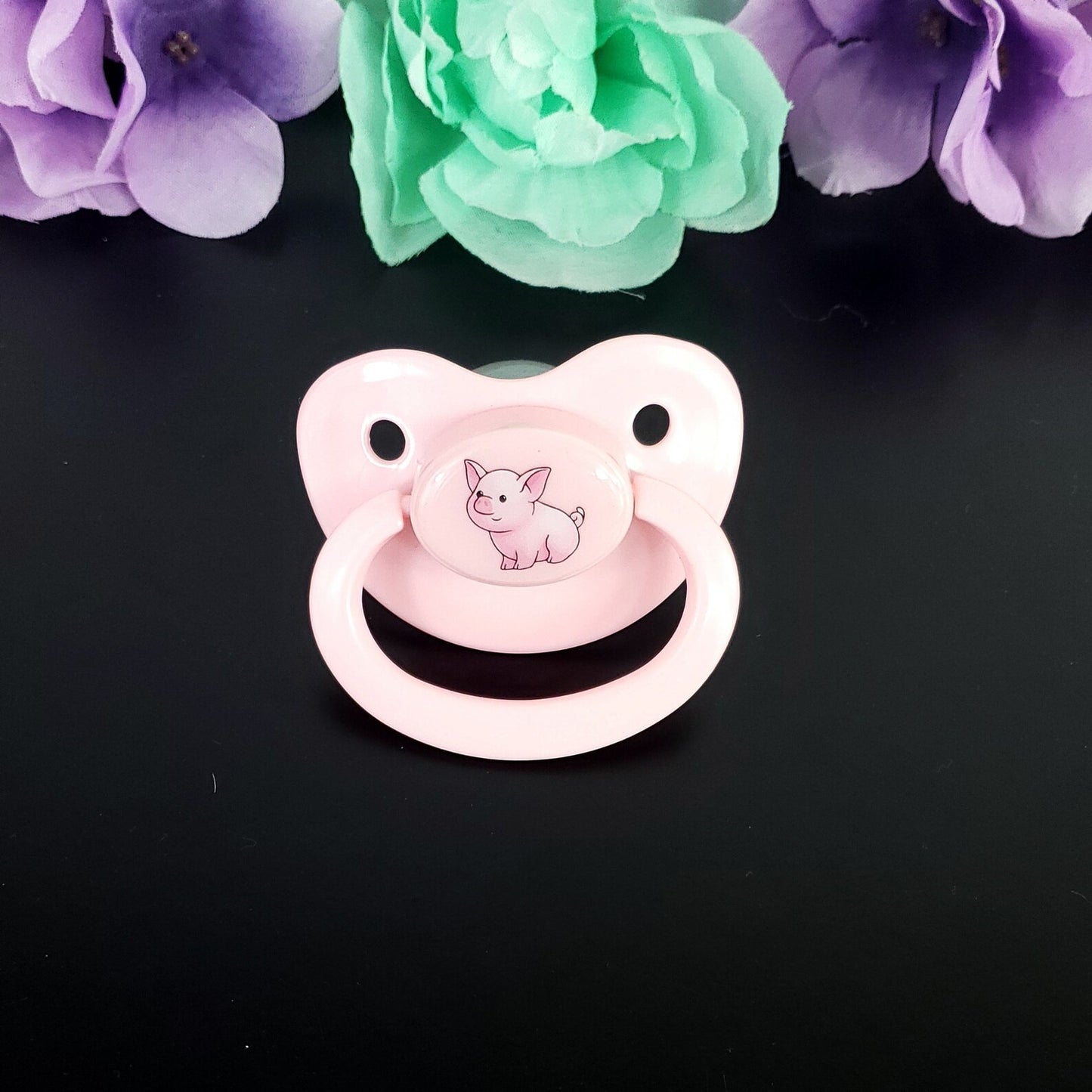 Pink pacifier with a pig design on a black background with flowers