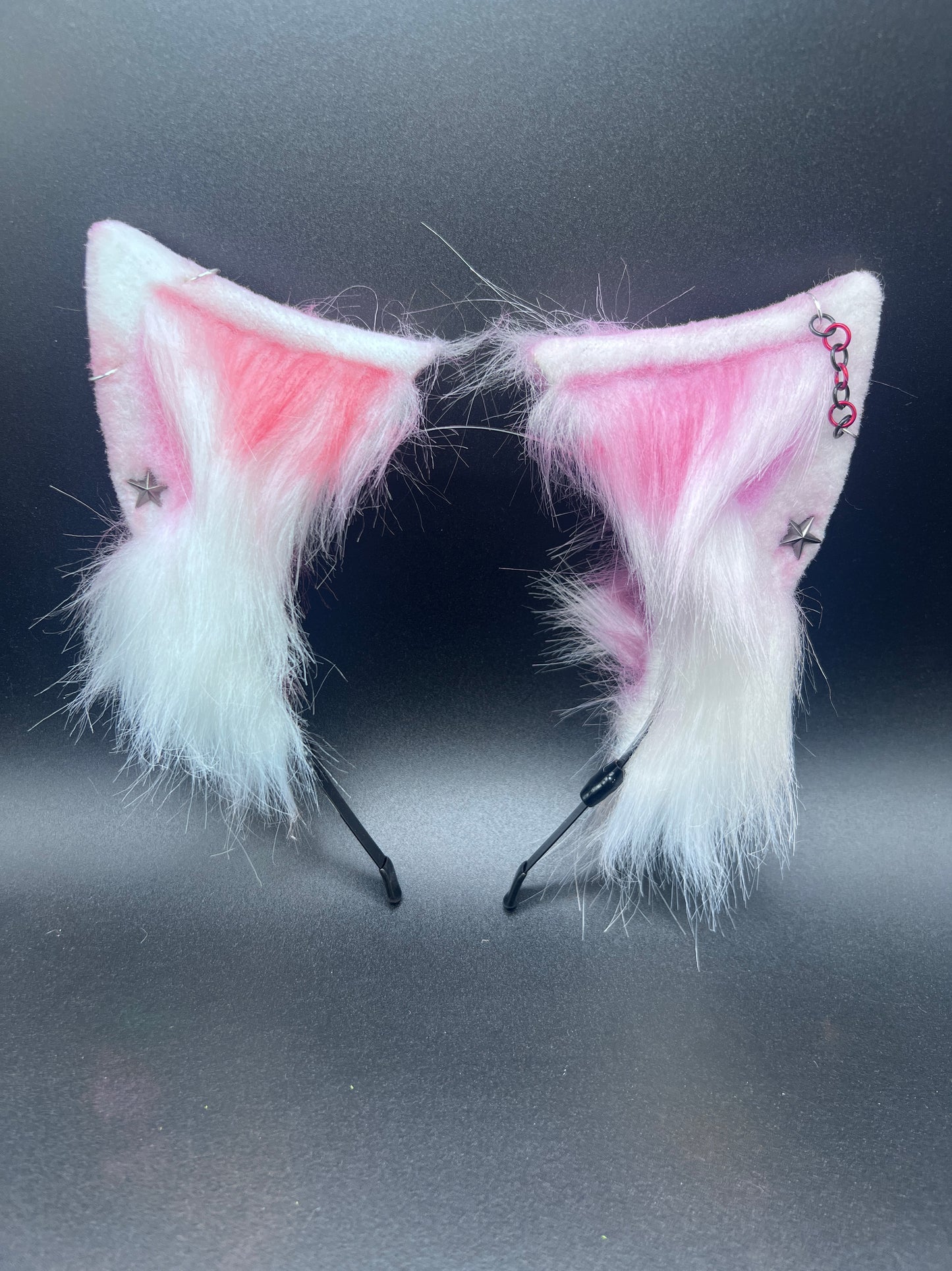 Pair of pink, red and white cat ears with earrings on a dark background