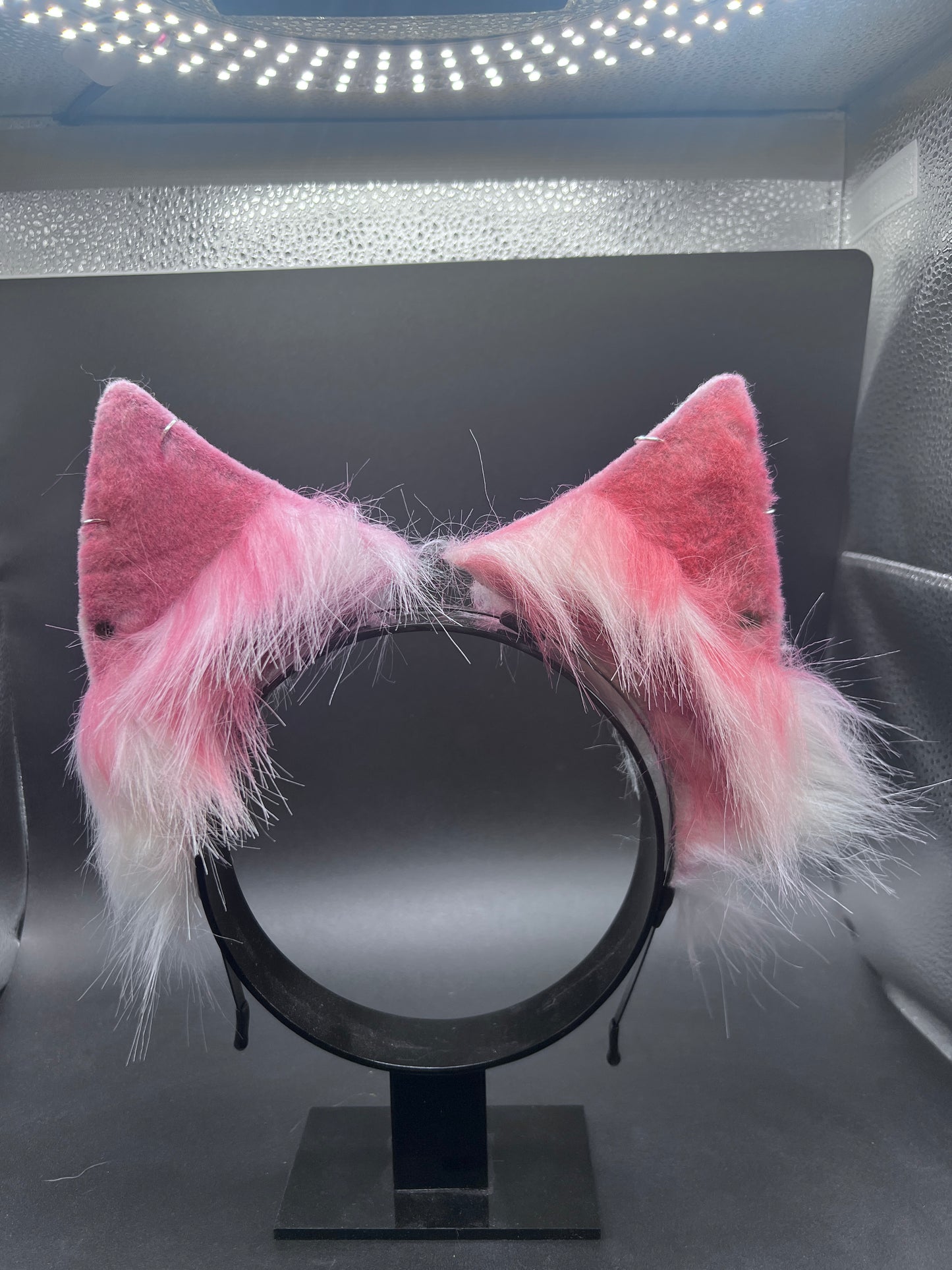 red and white fluffy cat ears on a black headband against a dark background