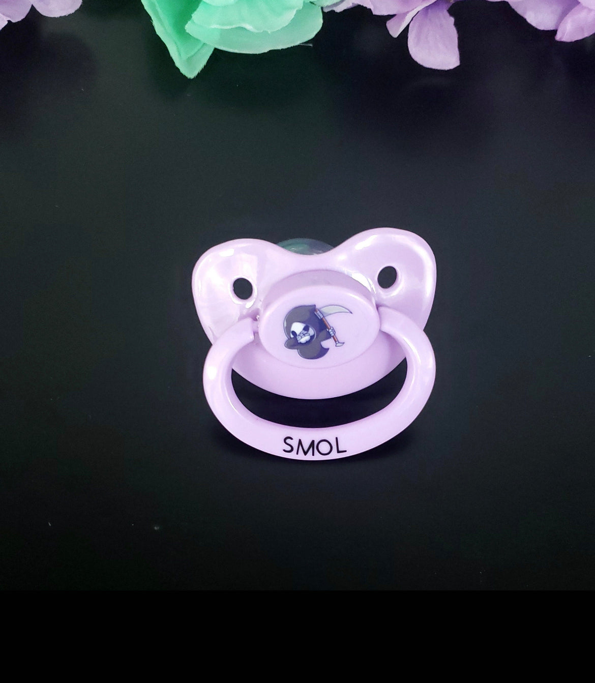 lavender adult dummy pacifier with kawaii grim reaper image on the center button with text on the handle that reads Smol