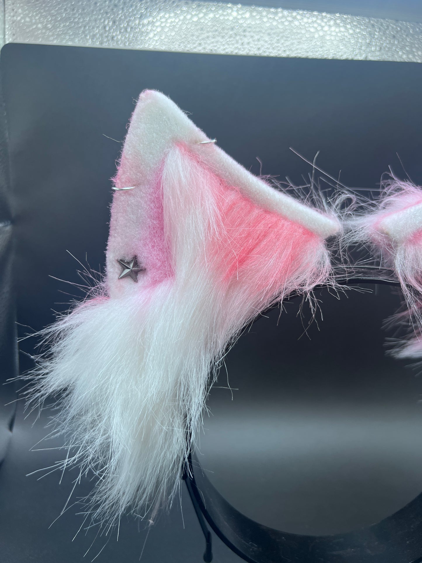 Pink and white furry ear with a star charm on a dark background