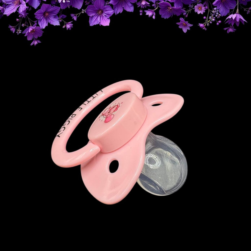 top down view of pink adult pacifier with pig image on button and Little Piggy text on handle