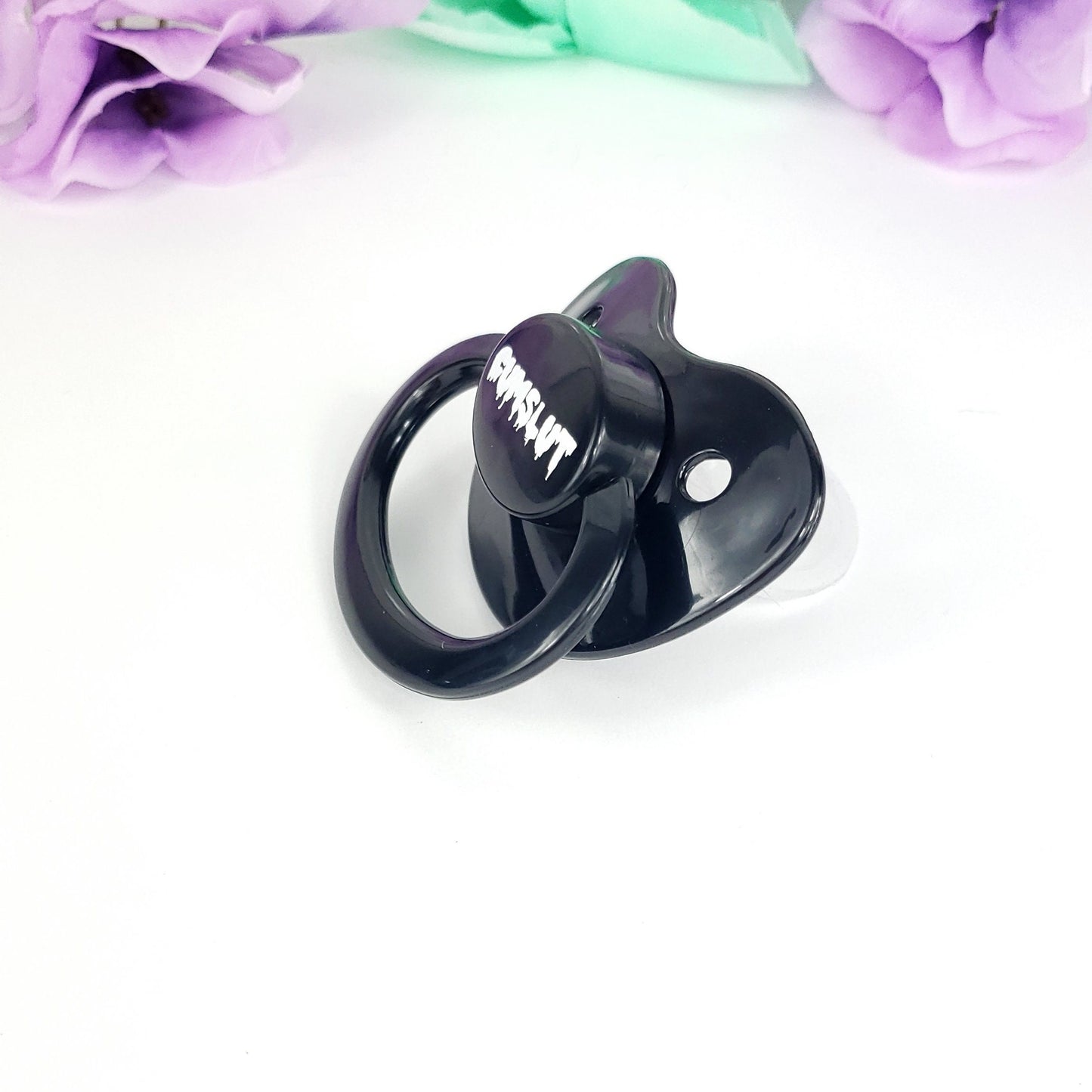A Purple adult pacifier featuring the word "Cumslut" boldly displayed in the center, designed for playful and cheeky self-expression.