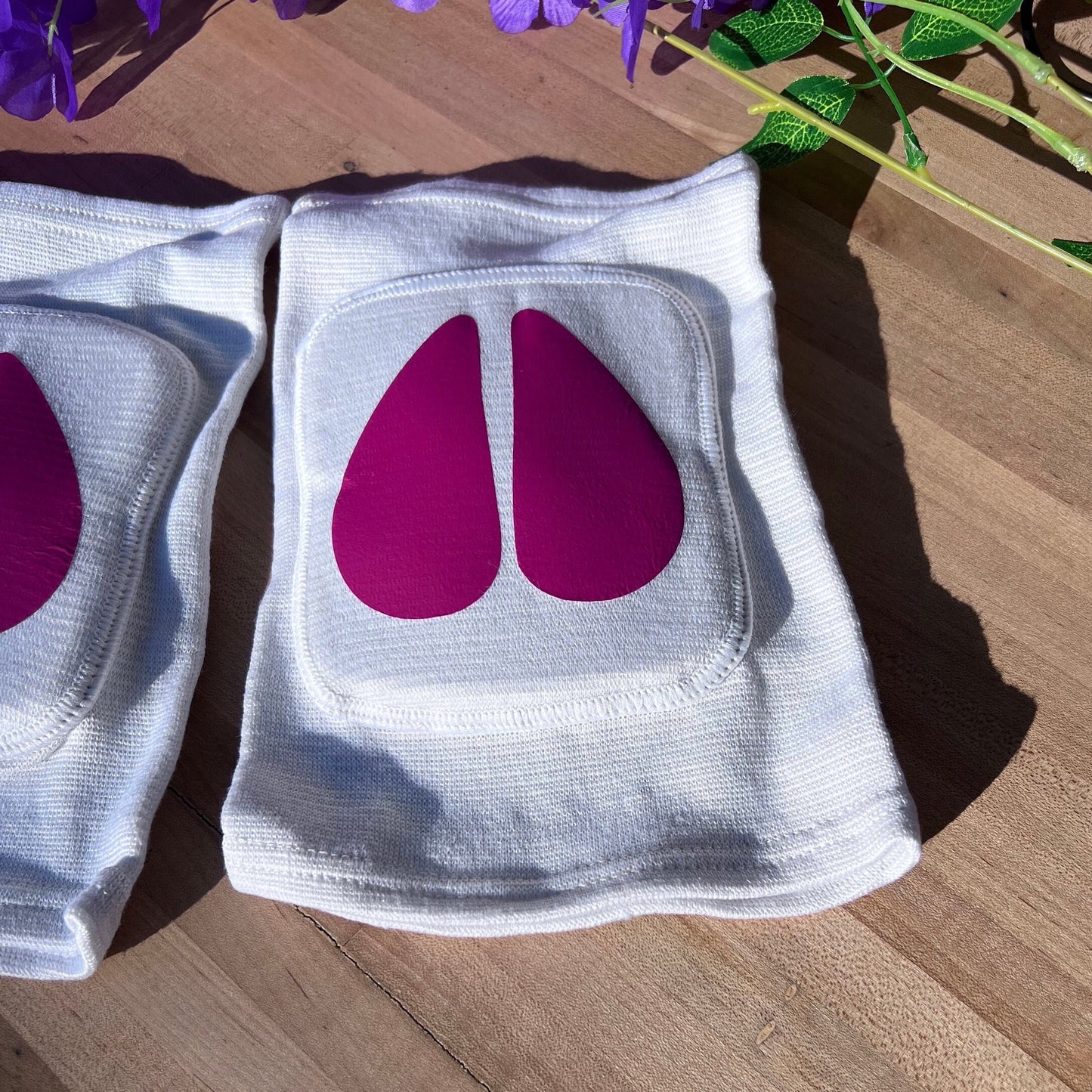Close-up of soft padded knee pad with hot pink cow hoof vinyl design on white base.