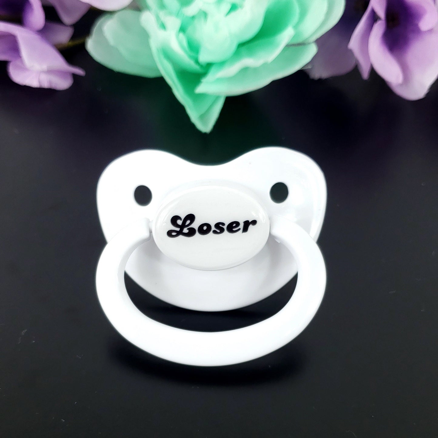 A white adult pacifier featuring bold black text in the center that reads "Loser," offering a simple and degrading design.