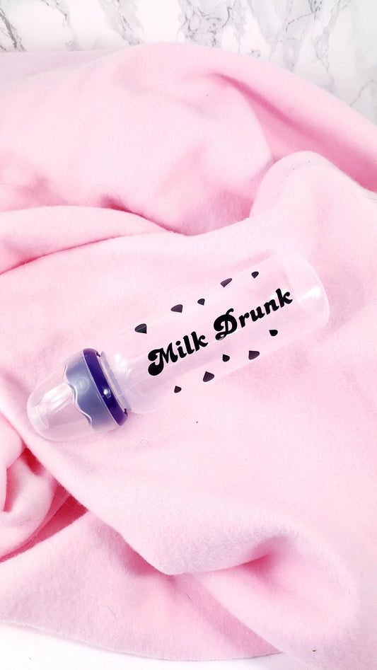 An 8oz adult baby bottle with the phrase "Milk Drunk" written in bold black text across with silhouette milk drops, offering a playful design.