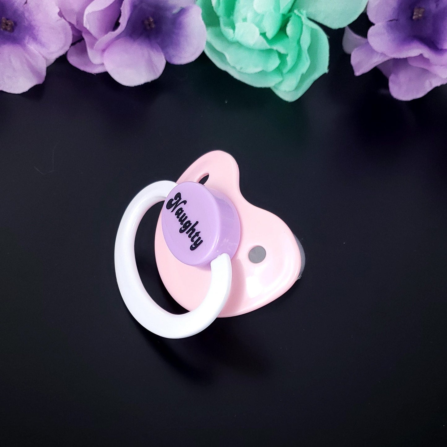 pastel adult pacifier with black text reading Naughty on the center button
