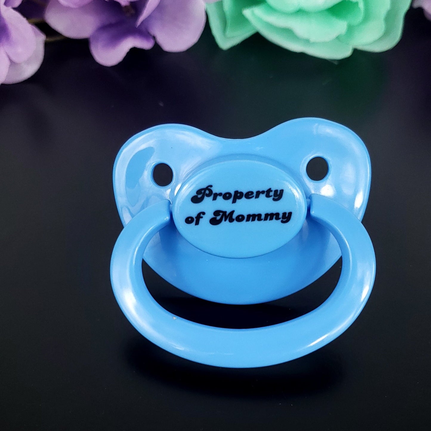 Baby blue adult pacifier with bold text saying "Property of Mommy" in the center, adding a playful and loving sentiment.