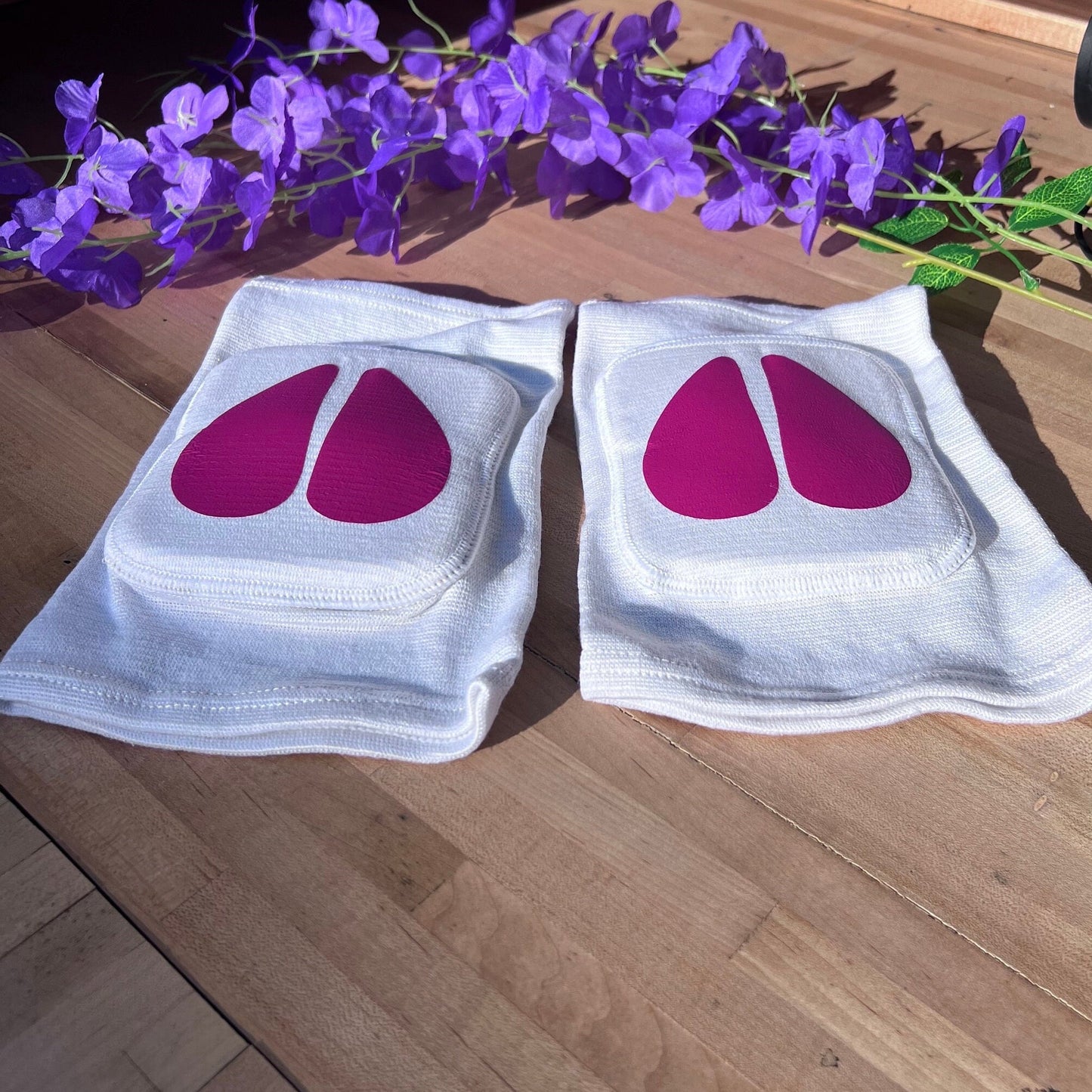 White cow hoof pet play knee pads with hot pink vinyl details, resting on wood background.