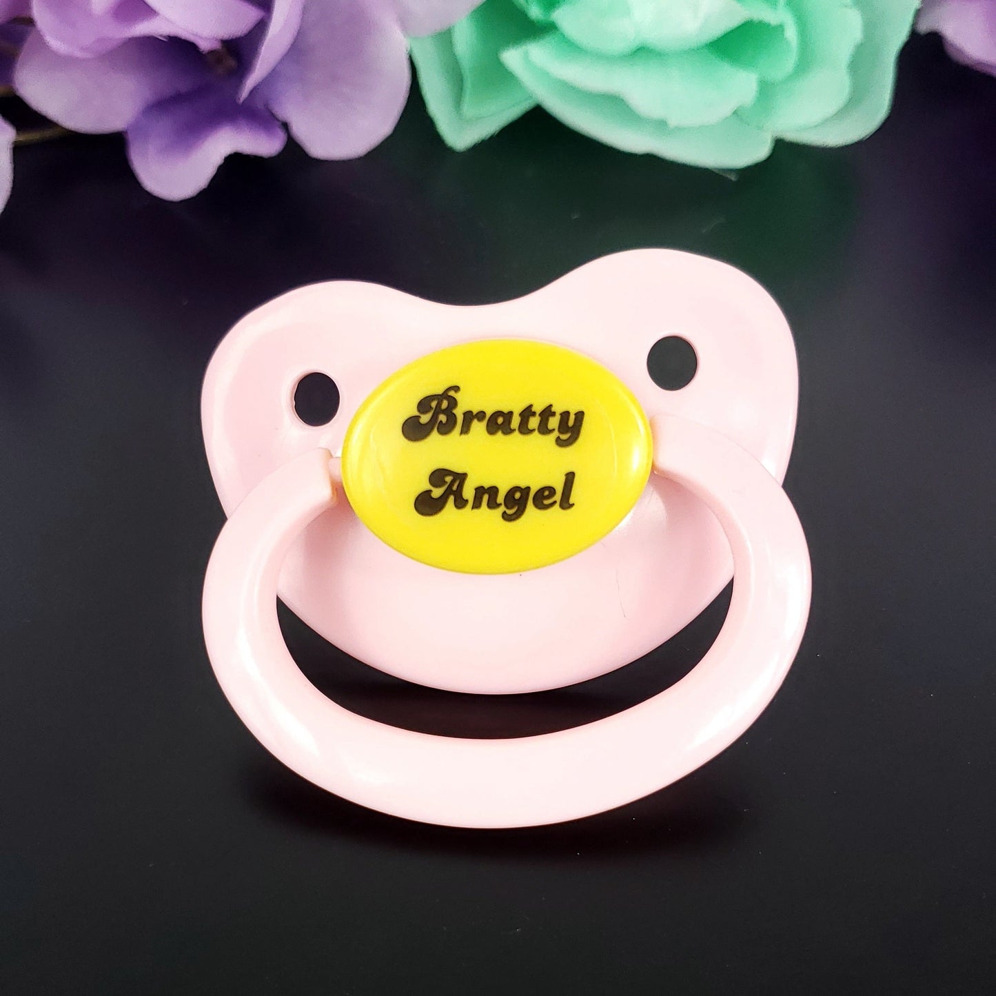 adult pacifier with the text bratty angel on the center button