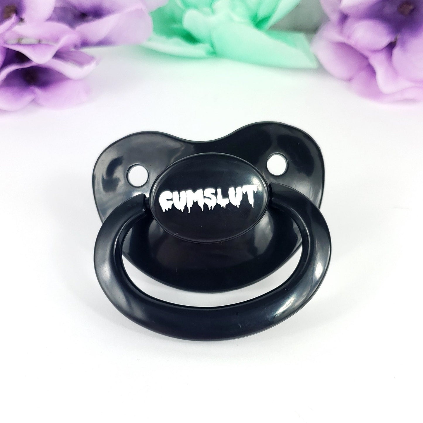 A black adult pacifier featuring the word "Cumslut" boldly displayed in the center, designed for playful and cheeky self-expression.