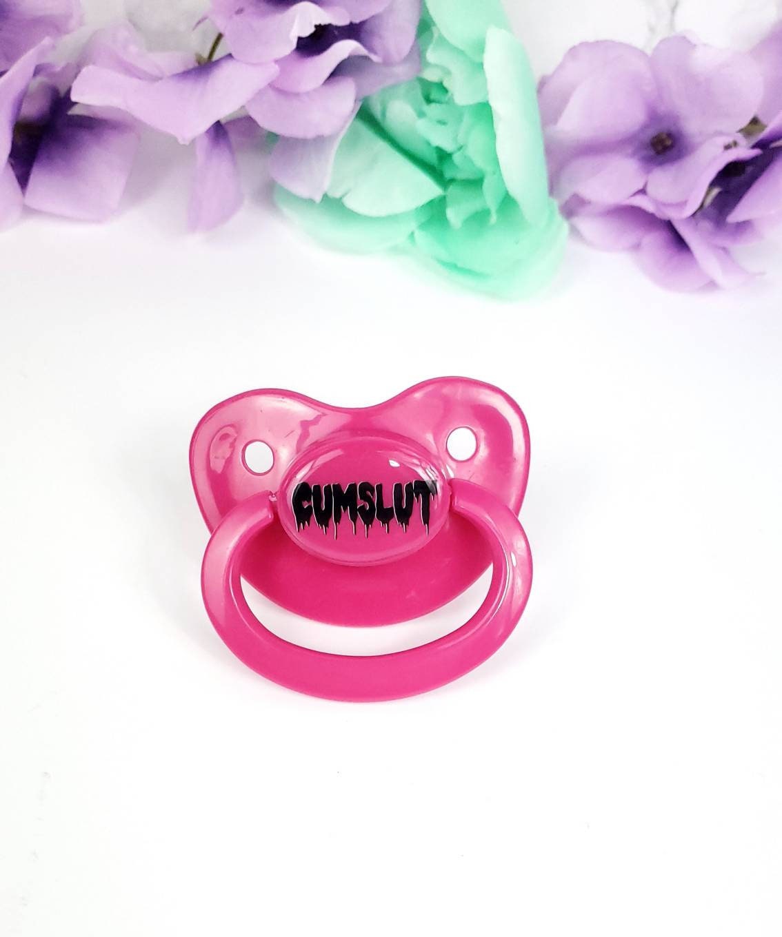 A hot pink adult pacifier featuring the word "Cumslut" boldly displayed in the center, designed for playful and cheeky self-expression.