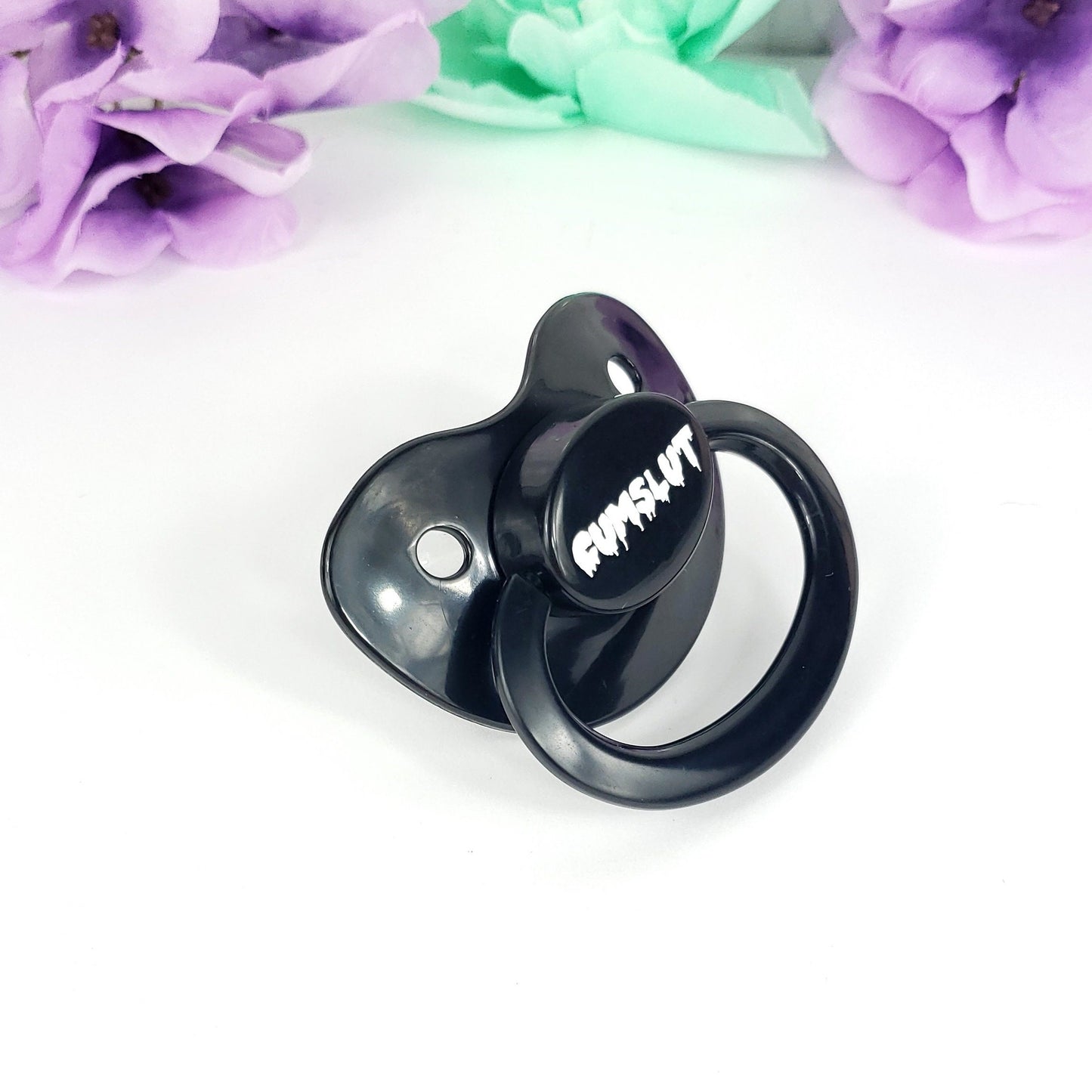 A Purple adult pacifier featuring the word "Cumslut" boldly displayed in the center, designed for playful and cheeky self-expression.