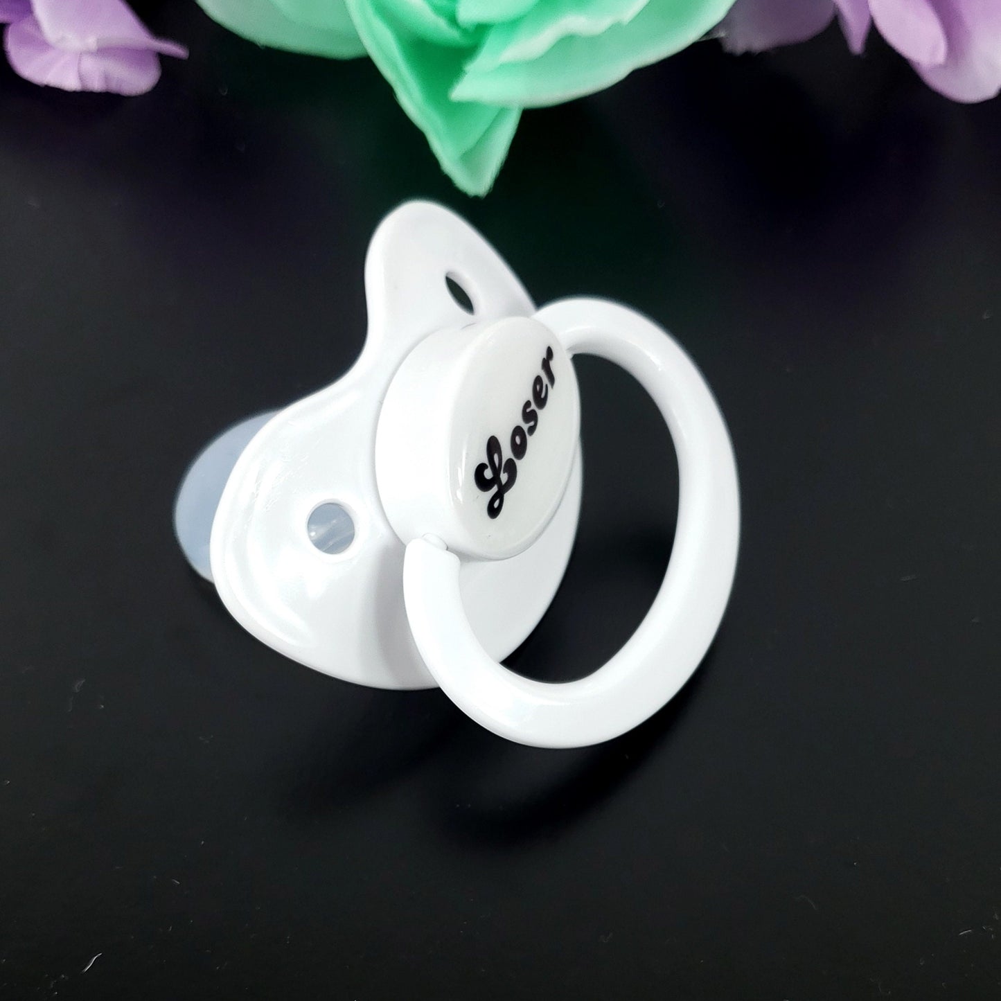 A white adult pacifier featuring bold black text in the center that reads "Loser," offering a simple and degrading design.