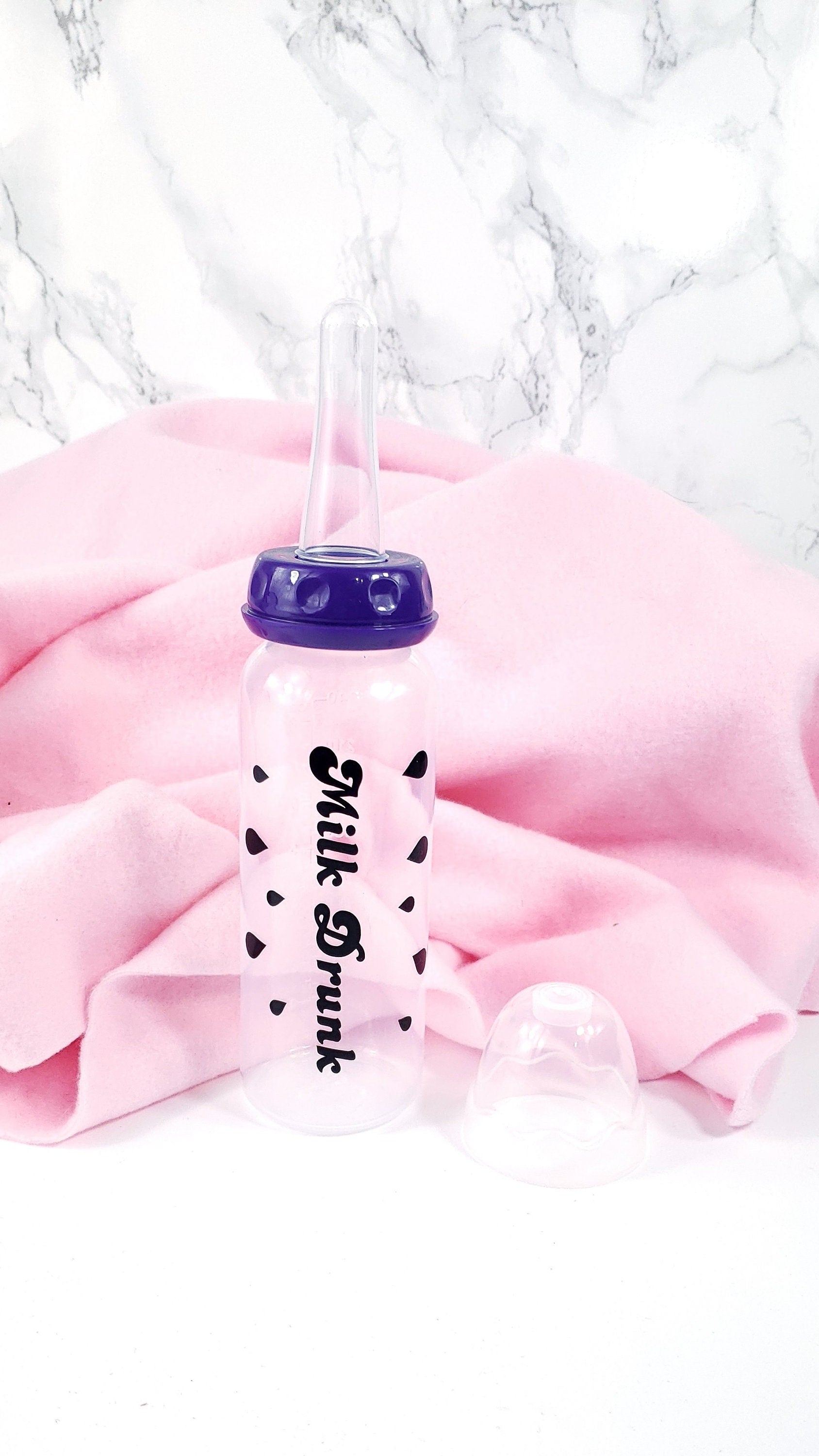 An 8oz adult baby bottle with the phrase "Milk Drunk" written in bold black text across with silhouette milk drops, offering a playful design.