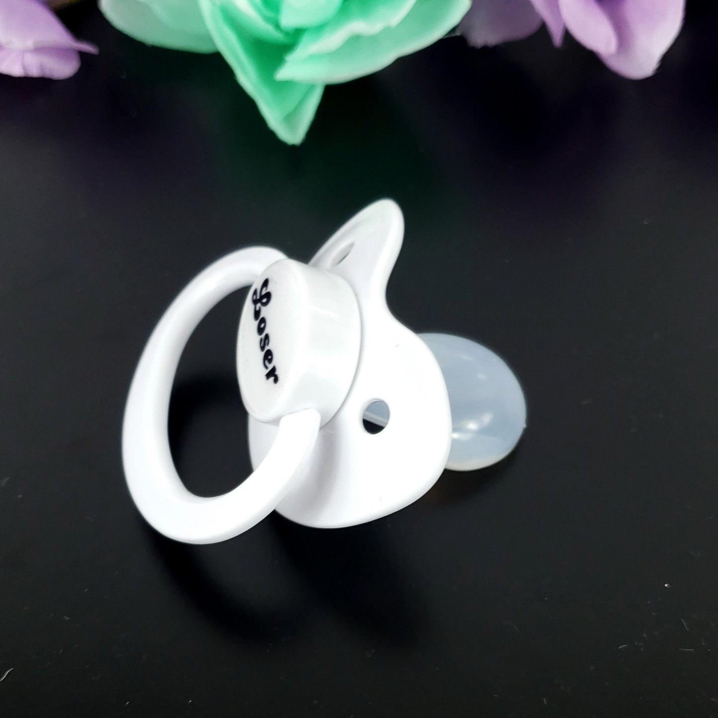 A white adult pacifier featuring bold black text in the center that reads "Loser," offering a simple and degrading design.