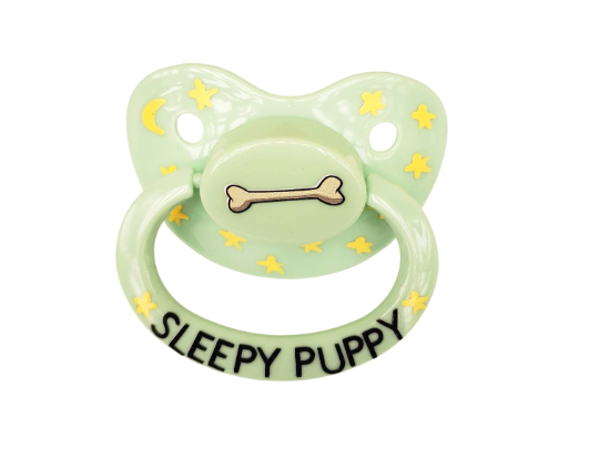 A green adult pacifier with yellow stars and a bone design, reading 'SLEEPY PUPPY' on the handle.