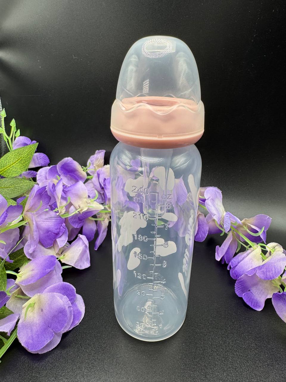 Adult Baby bottle with pink cap on a black background with purple flowers