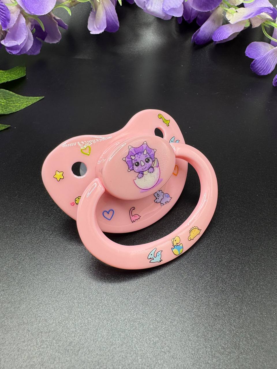 pink adult pacifier with baby triceratops button and glow in the dark deco images on shield and handle