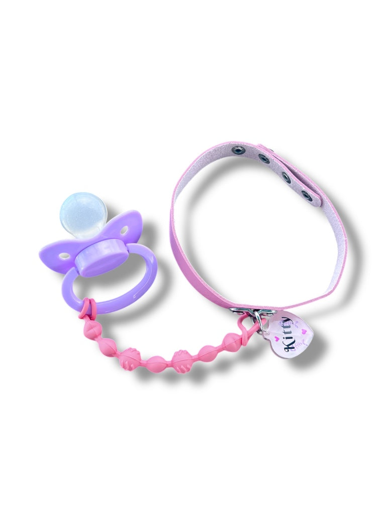  pink choker with a resin tag that reads "Kitty." A pink chewable pacifier clip is attached to the choker, ending in a lavender adult pacifier.