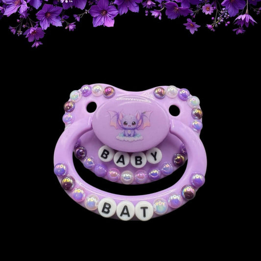 Purple bat-themed adult pacifier with text beads spelling 'Baby Bat,' surrounded by various shades of purple pearls for a cute and gothic aesthetic.