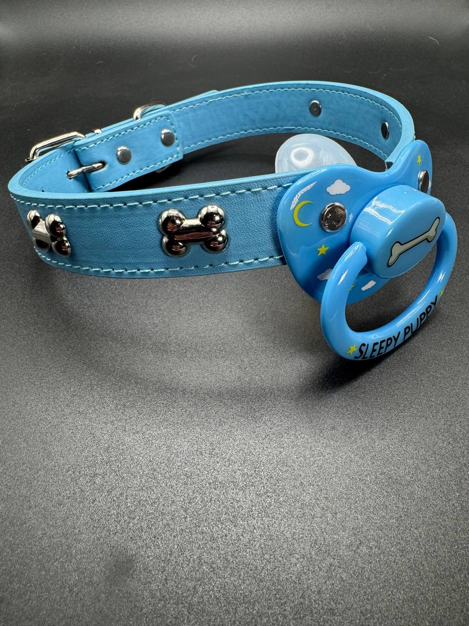 Blue pet play pacifier choker with silver dog bone embellishments. Pacifier has a dog bone center with clouds and stars on the shield and the text Sleepy Puppy on the handle