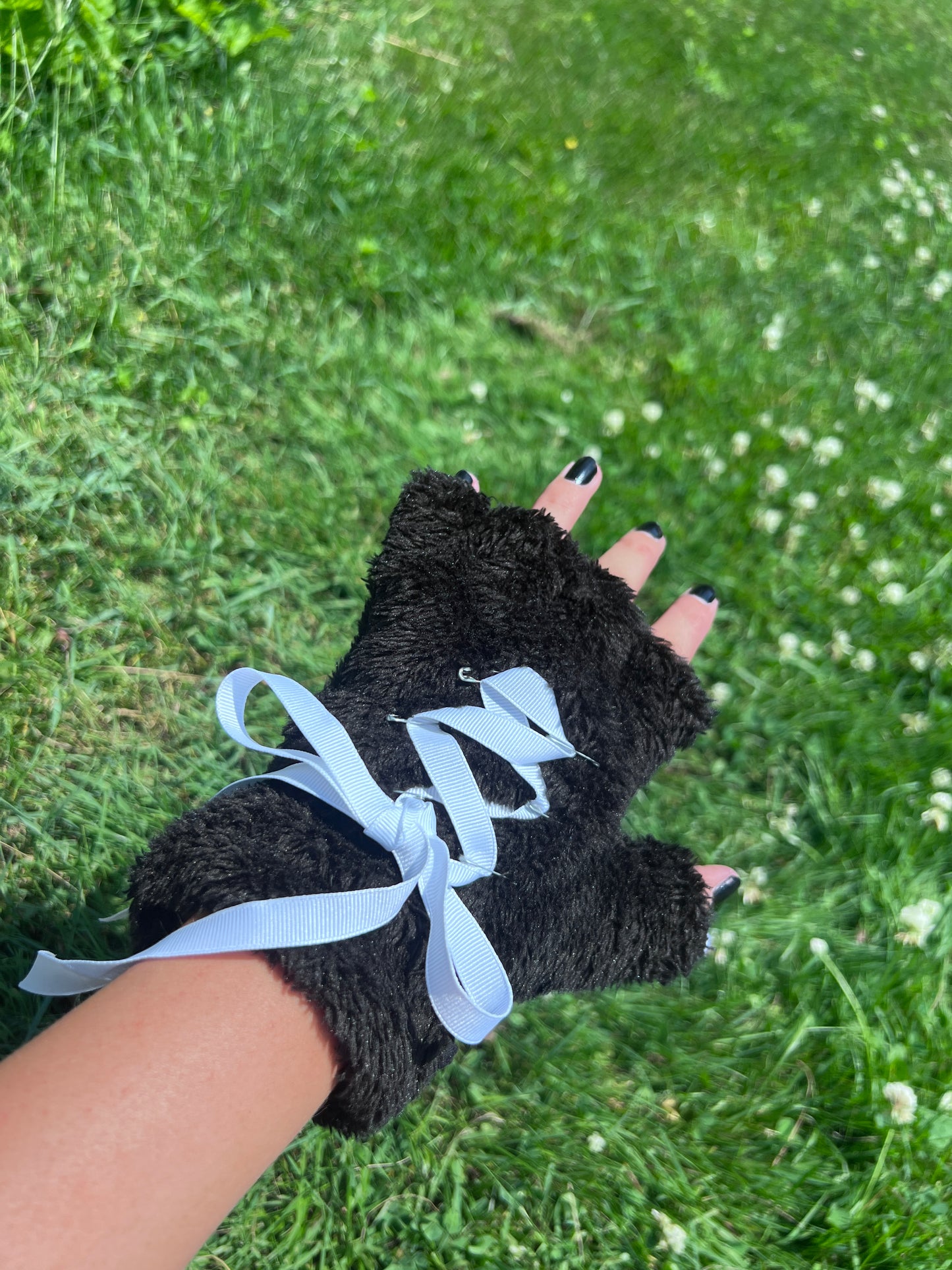 black paw gloves with white ribbon lace up back against green grass
