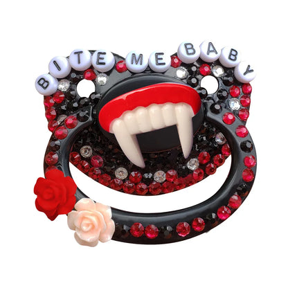 A black adult pacifier adorned with black and red gems, featuring fangs in the center and the text "Bite Me Baby" elegantly displayed along the top, creating a bold and edgy design.