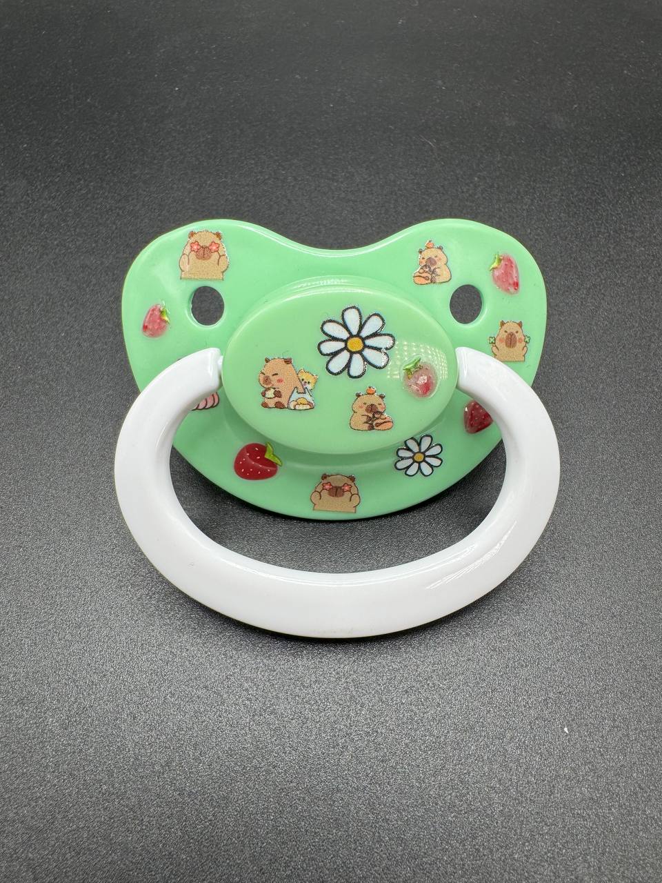 Green adult pacifier with capybara and flower designs on a gray background