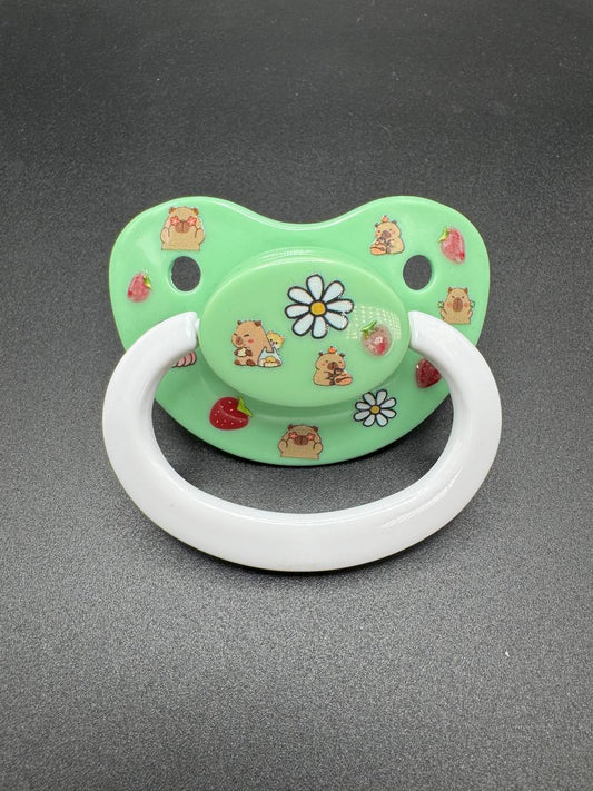 Green adult pacifier with capybara and flower designs on a gray background