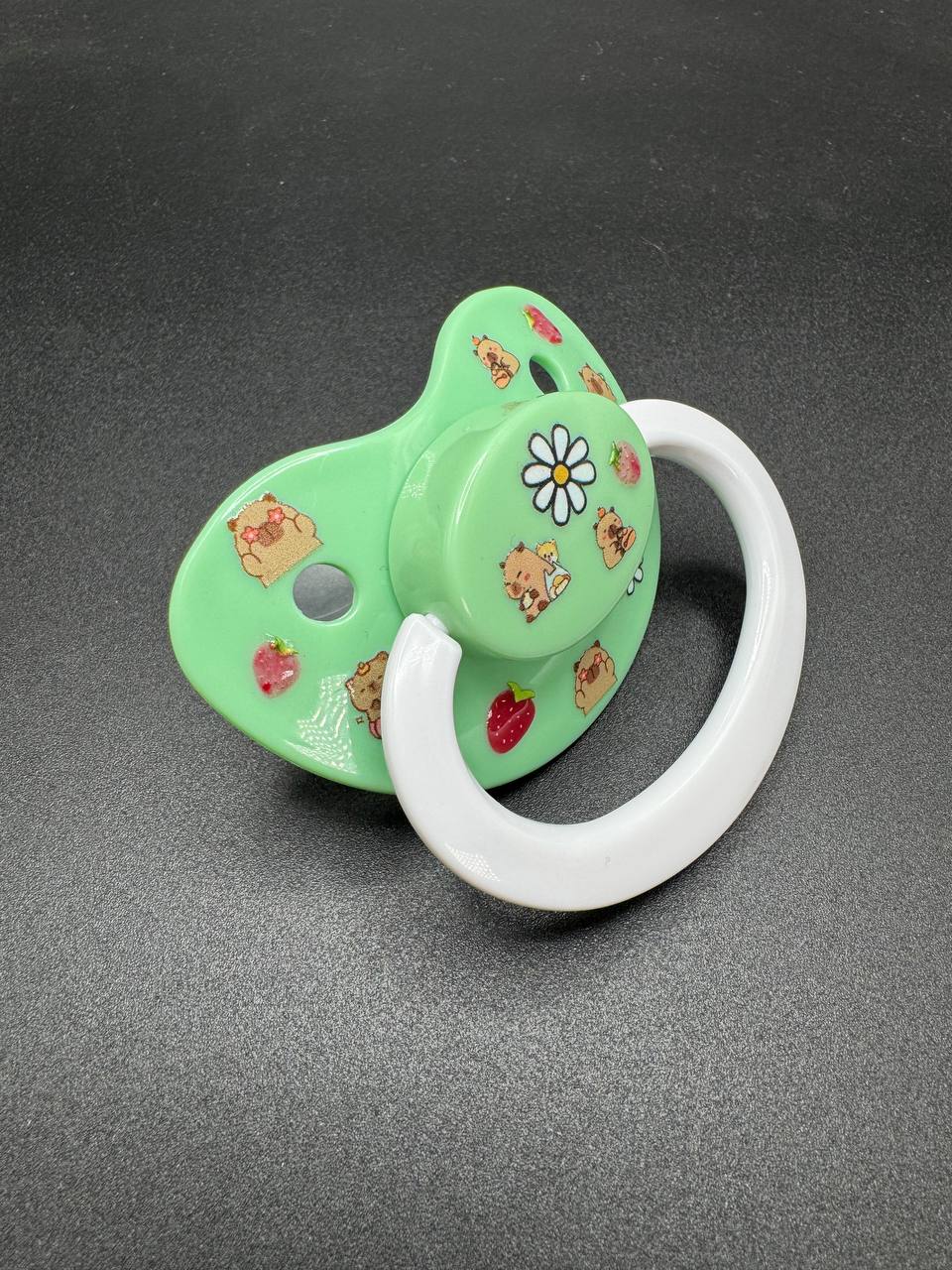 Green ABDL pacifier with cartoon capybara characters and flowers on it