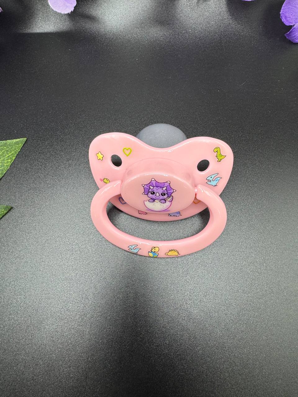 Deco adult pacifier with triceratops and other dinosaurs decorating the pacifier